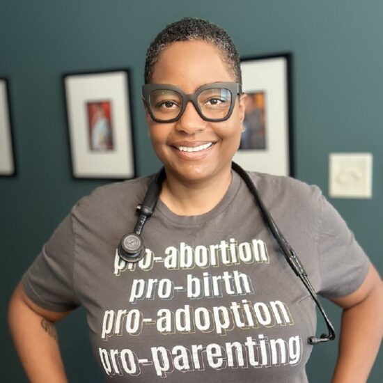 A woman smiles at the camera wearing a stethoscope around her nexk and a t-shirt that reads: pro-abortion, pro-birth, pro-adoption, pro-parenting