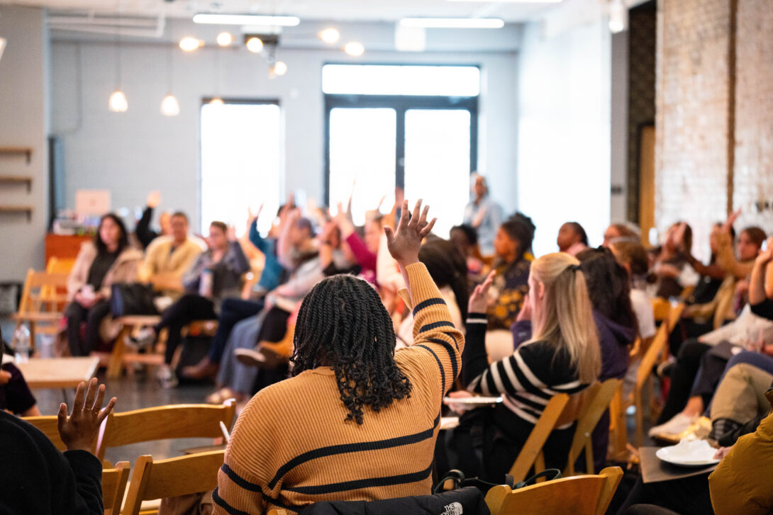 A room full of people, shot from the side, many raising hands