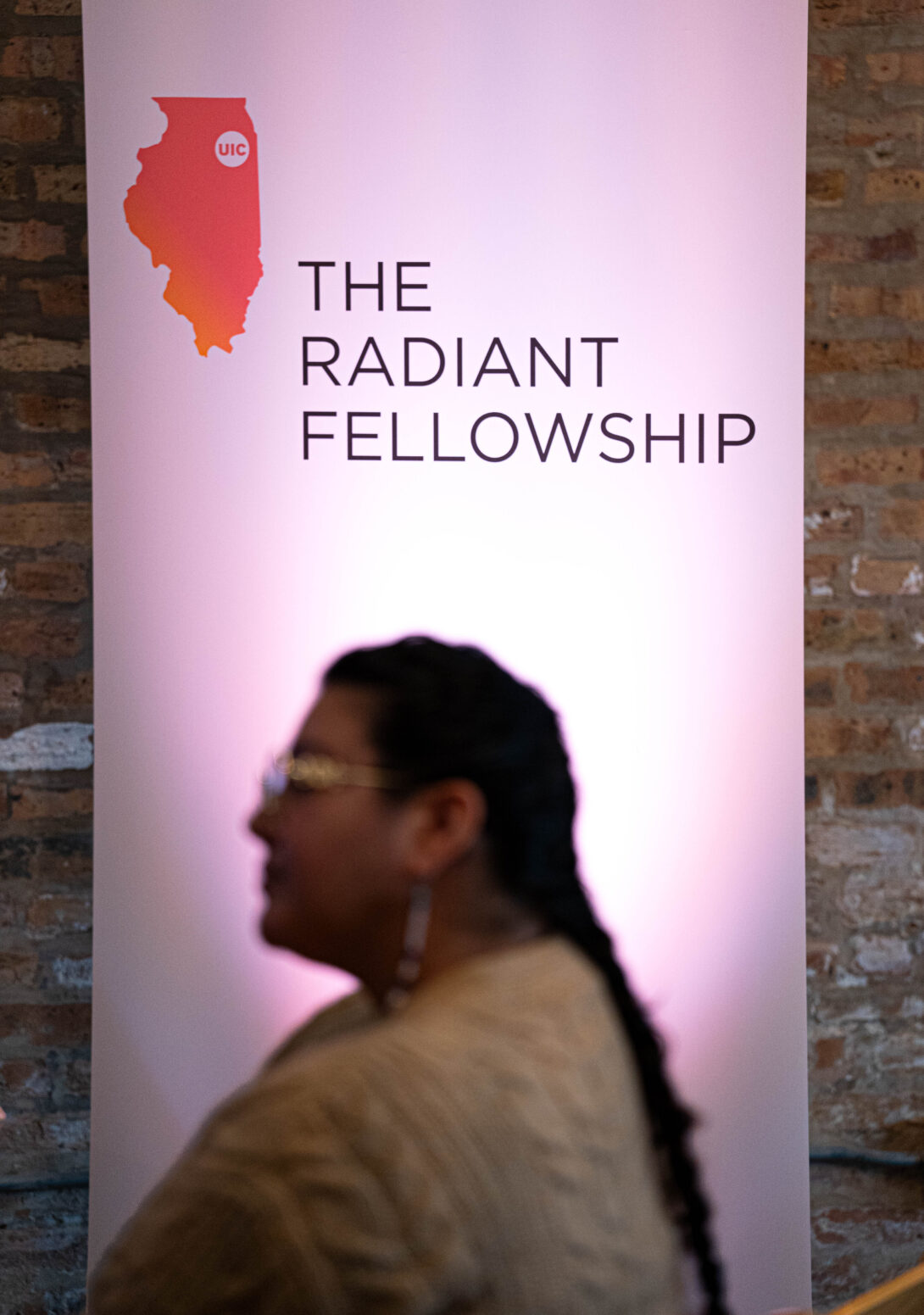 woman with a long braid and glasses sits in front of an illuminated sign that reads, 